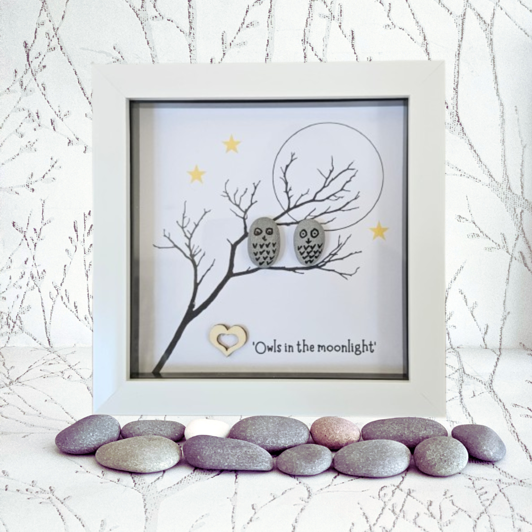 Framed artwork with two owls on a branch, surrounded by pebbles and branches in the foreground.