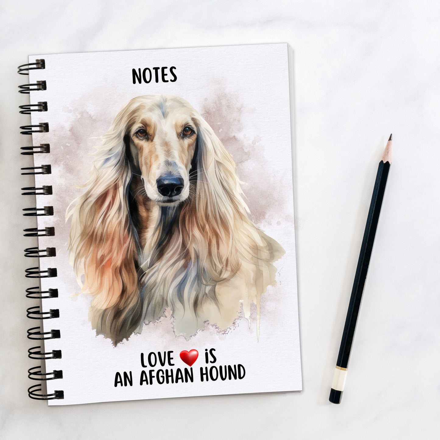 Spiral bound notebook in white showing the head shot of an Afghan Hound with flowing hair facing forward on a smoky background and a quote written at the bottom. A black pencil is placed to the right hand side.