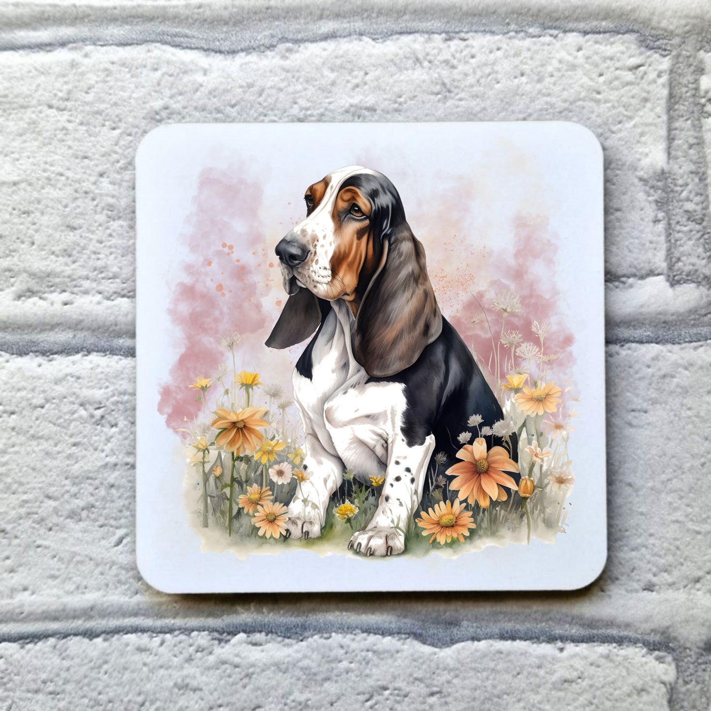 White drinks coaster with a Tri-coloured Basset Hound sat among orange flowers with a smoky pink background. The coaster is placed on a grey, brick effect surface.