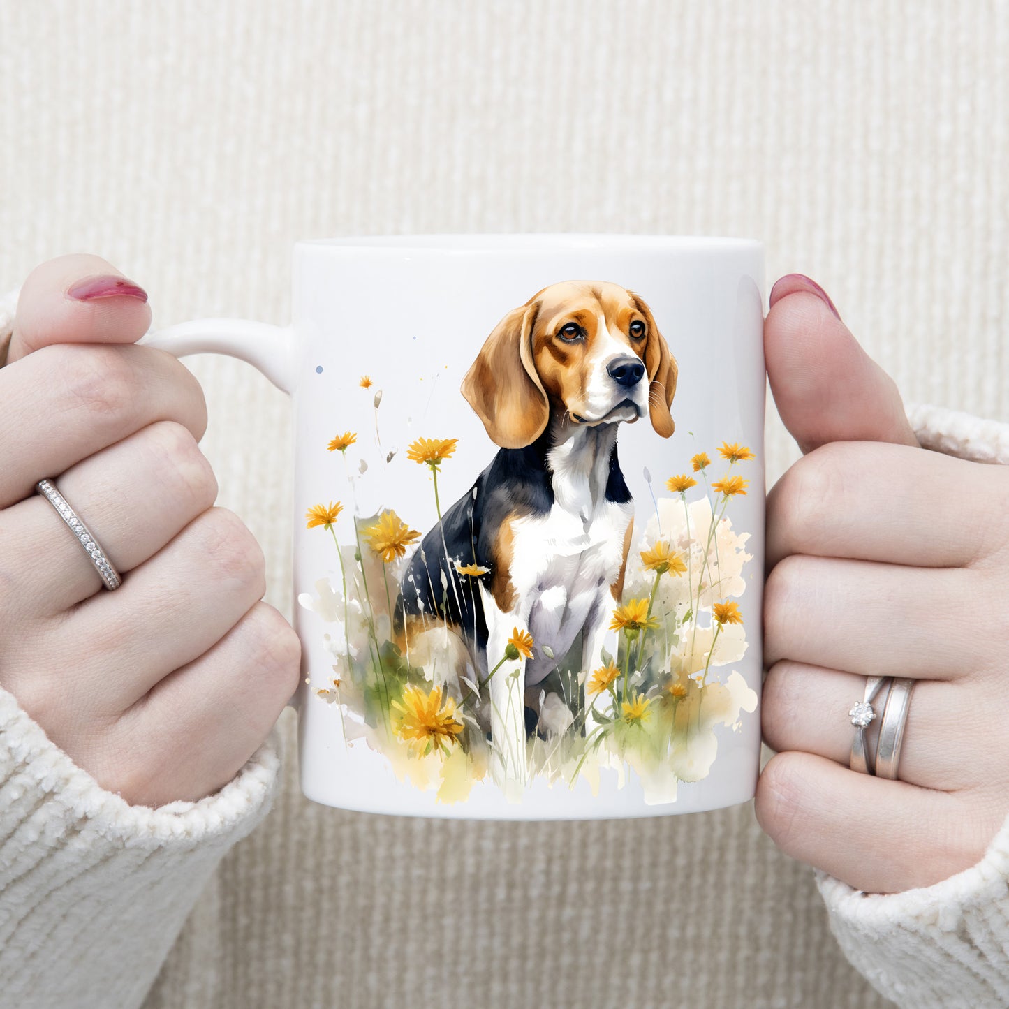 A Beagle dog is sat facing right among yellow wildflowers on a white ceramic mug. A woman is holding the mug with both hands.