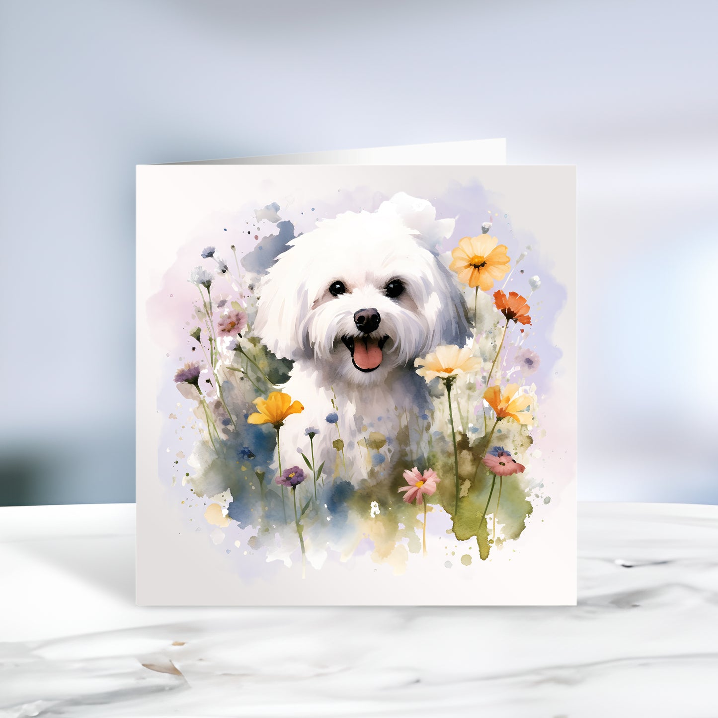White card featuring a vibrant printed image of a Bichon Frise dog sat among various flowers and with a lilac smokey background. The card is placed on a grey marble surface.