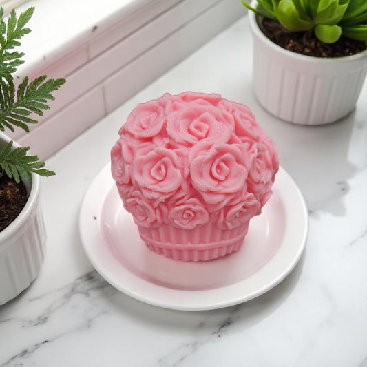 Pink rose-patterned wax melt on a white plate with plants in the background