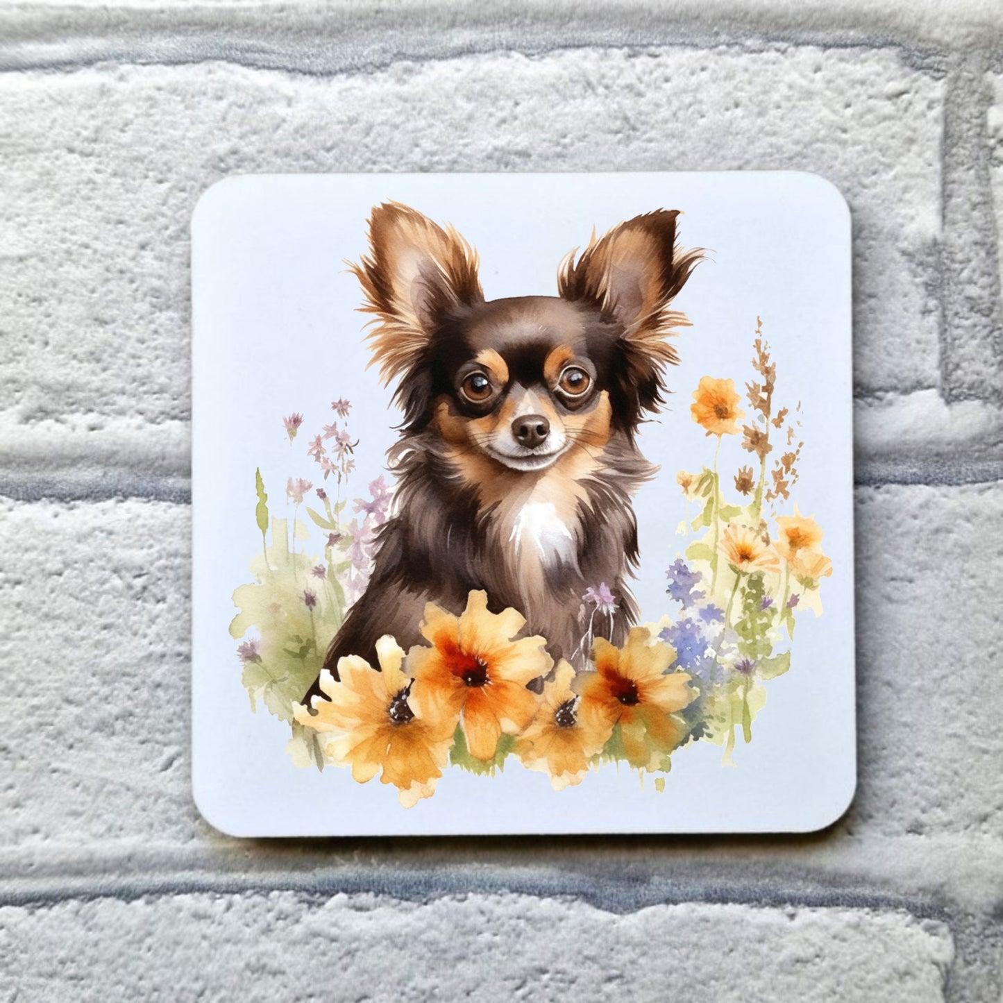 White coaster featuring a printed image of a liver and tan Chihuahua sat among flowers. Coaster is placed on a grey brick surface