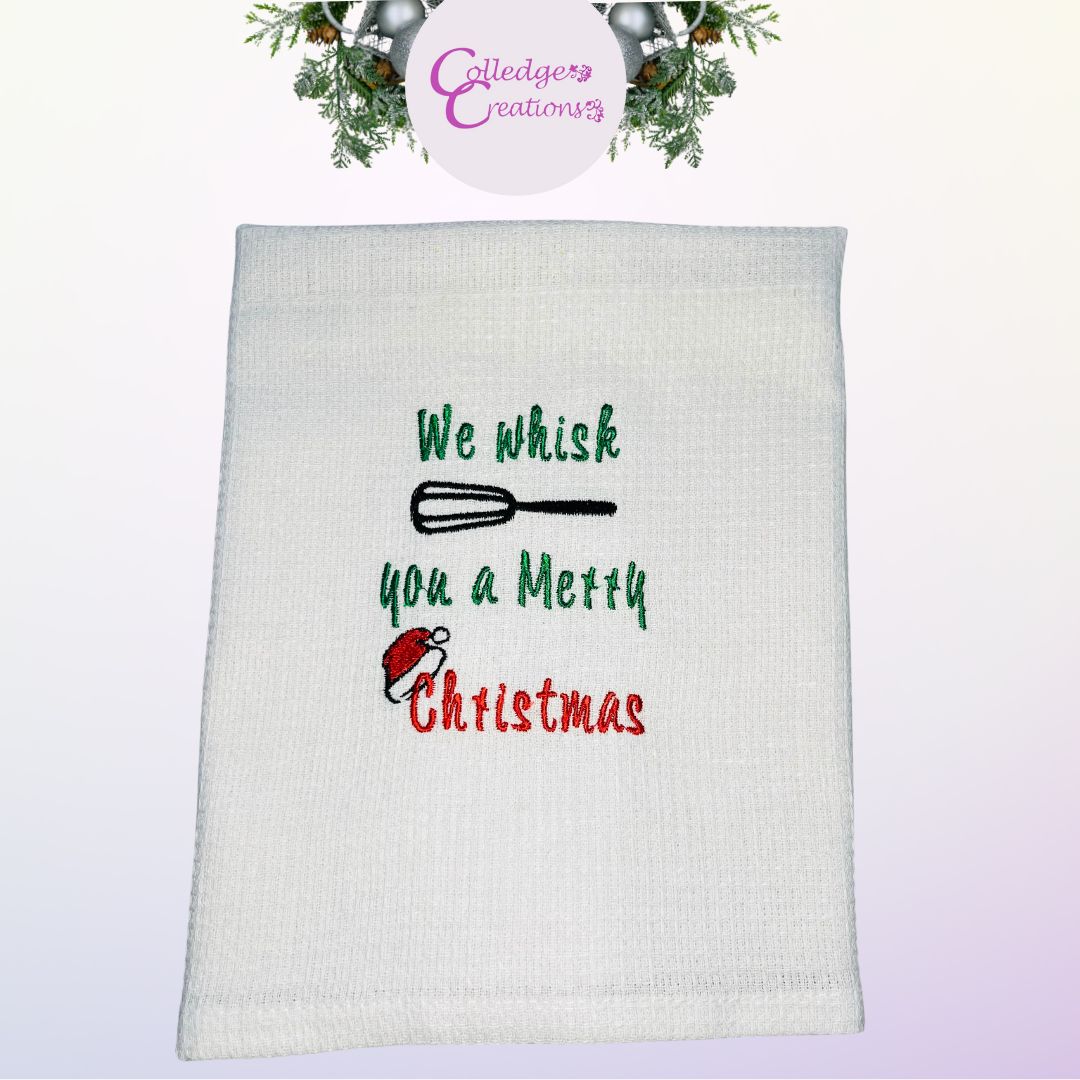 Image of embroidered Christmas tea towel with an embroidered Santa hat and a whisk saying we whisk you a Merry Christmas