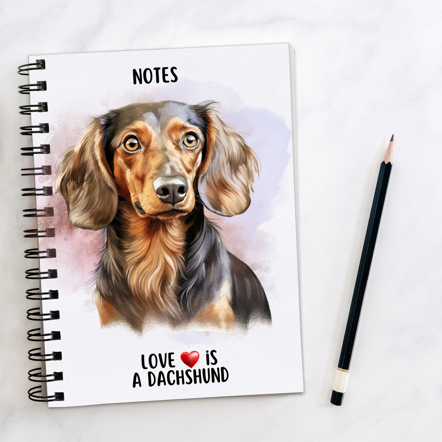 A5 white spiral bound notebook with a liver and tan Dachshund on the front. Black wire binding and a black pencil to the right hand side. A quote with a red heart is placed at the bottom of the book.