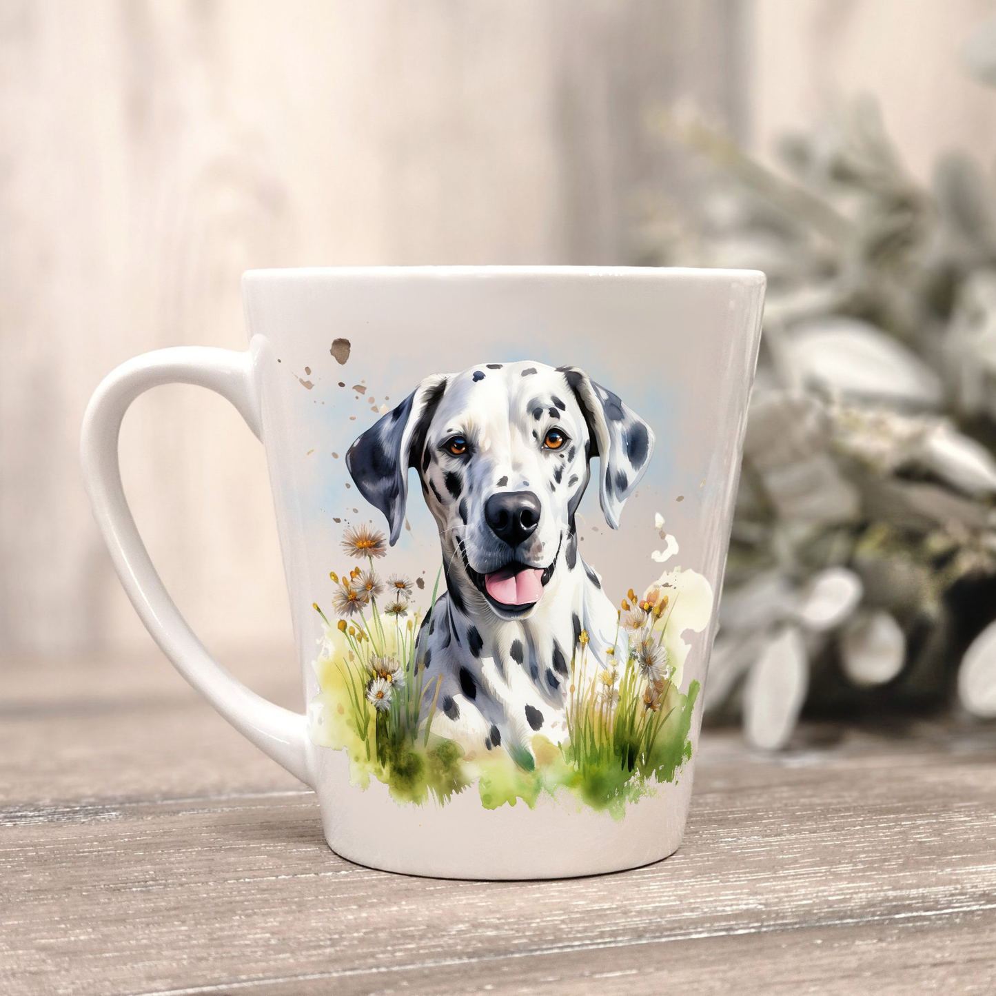A Dalmatian is shown lying on a white ceramic latte mug sat among wildflowers. The mug is placed on a wooden surface with sage green foliage to the right-hand side.