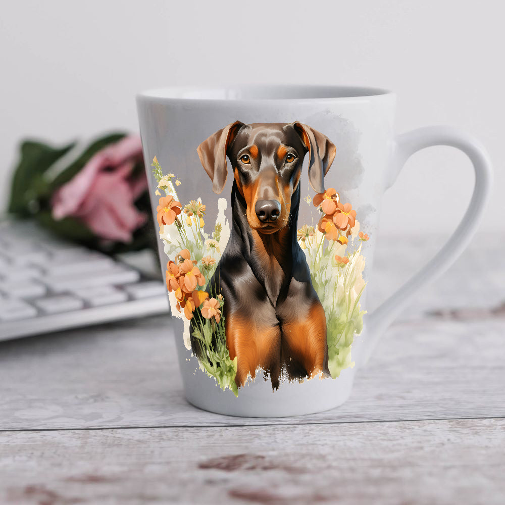 A 12oz white ceramic latte mug with a printed image of a tan and liver Doberman facing forward and sitting among flowers. A computer keyboard sits in the background. The mug is positioned on a wooden surface.