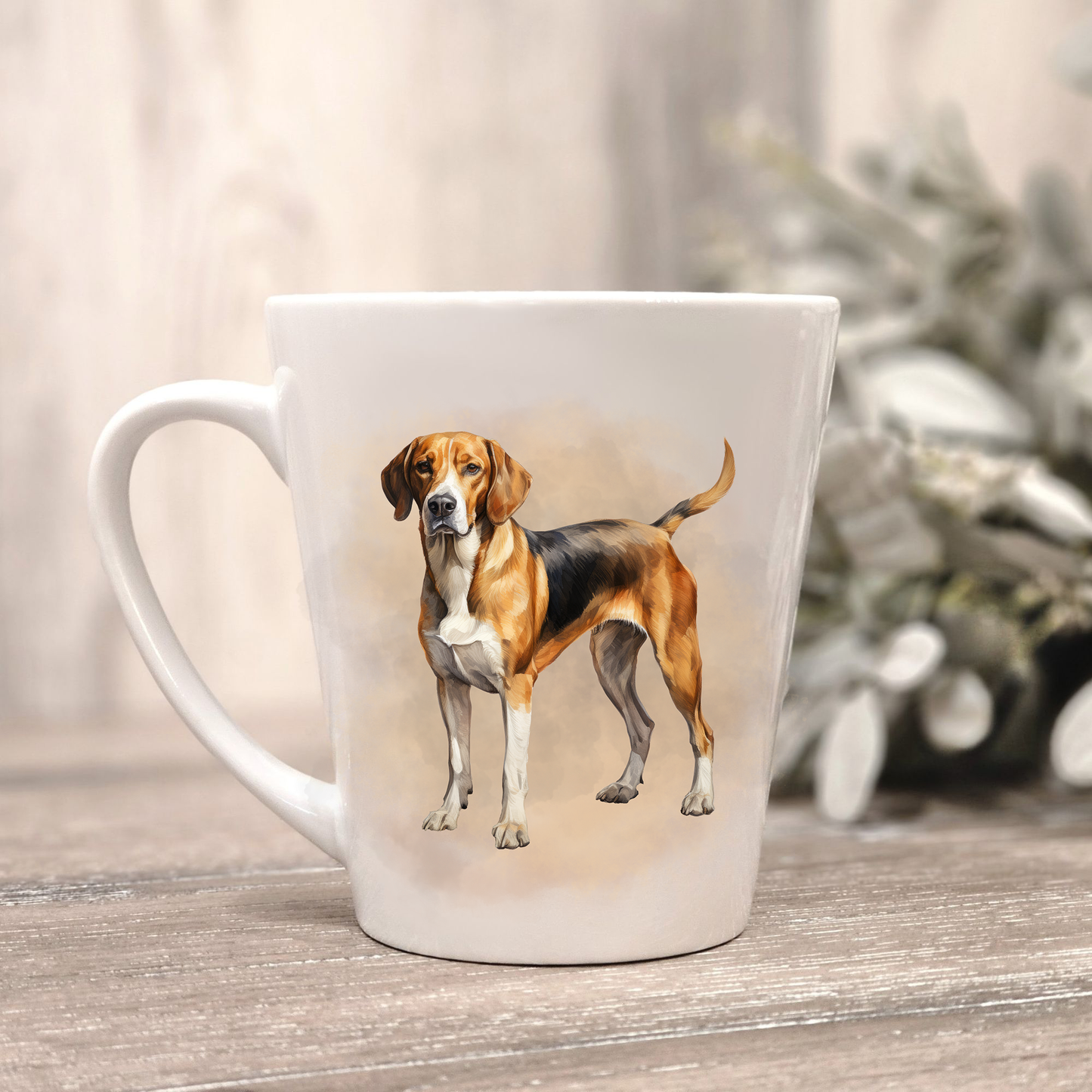 A Foxhound stands on a white ceramic latte mug in a smoky background and looking forward. The mug is placed on a wooden surface with sage green foliage to the right-hand side.