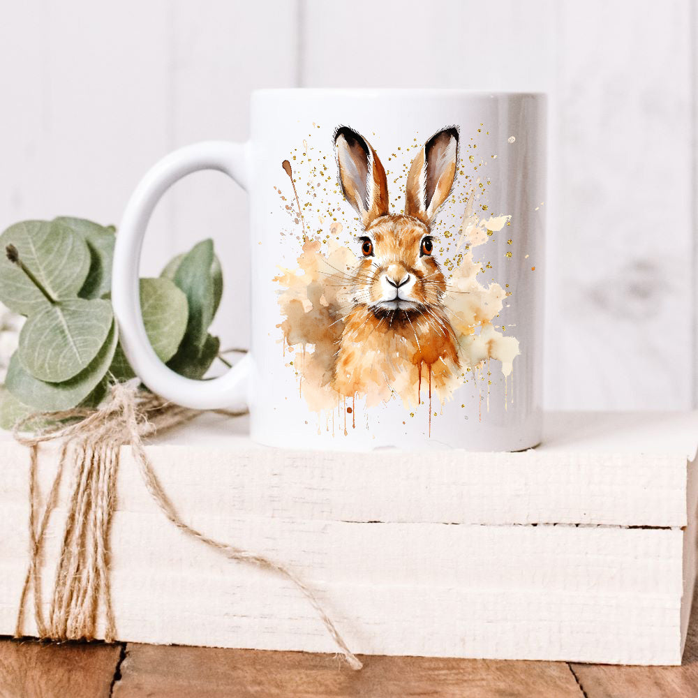 A brown hare sit facing forward on a white ceramic mug. A brown smoky background with splatters decorates. The mug is placed on a white wooden box and green leaves decorate the box with rustic string.