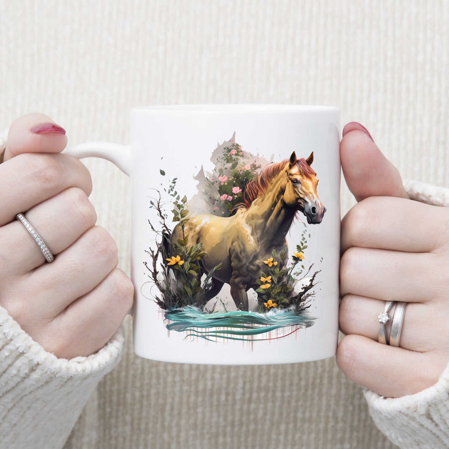 A sandy coloured horse standing in water with yellow and pink flowers decorating. Image on a white ceramic mug being held with both hands by a woman.