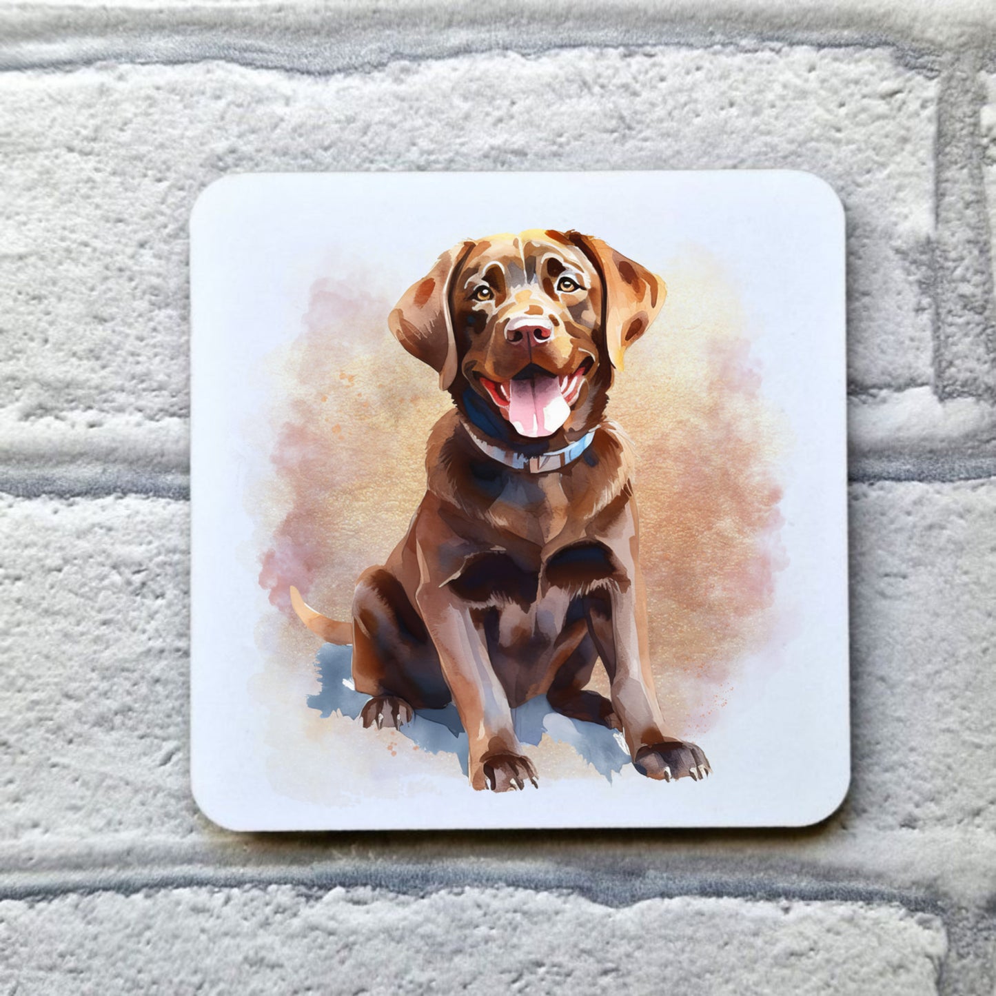 A Chocolate Labrador with mouth open and tongue out is sitting facing facing forward among a pink and gold misty background on a white coaster. The coaster is placed on a grey, brick effect surface.