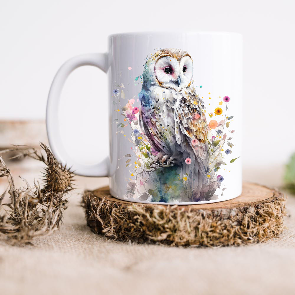 A Barn Owl sits perched among colourful wildflowers looking to the right on a white ceramic mug. The mug is placed on a thick wooden disc and a dried thistle is set to the left hand side.