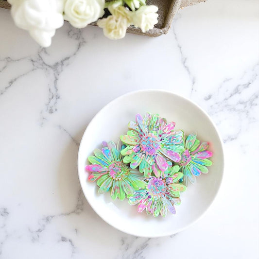 Colorful flower-shaped wax melts on a white plate with white flowers in the background