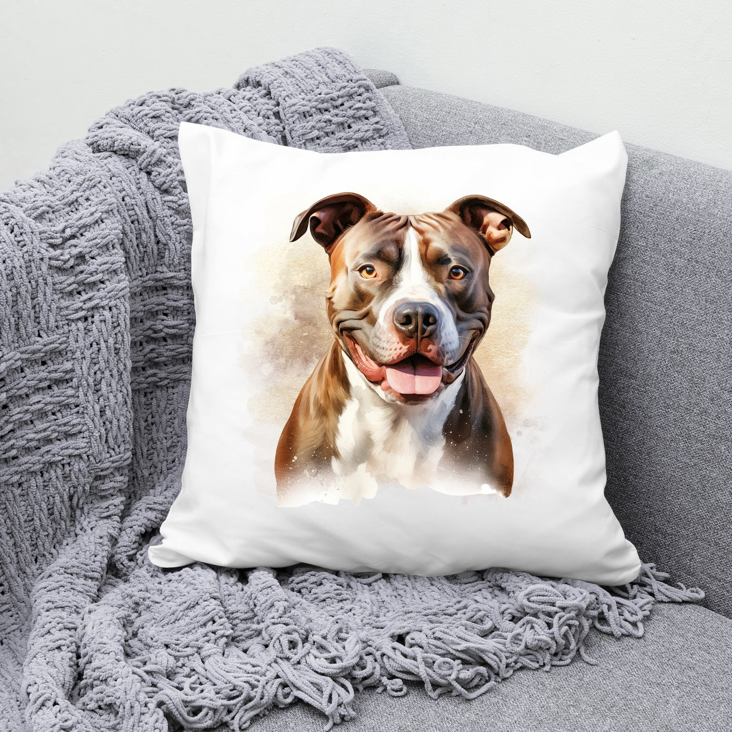 White sofa cushion with an image of a brindle Staffordshire Bull Terrier with a white chest sat facing forward. The cushion is placed on a grey sofa with a grey blanket draped across the corner