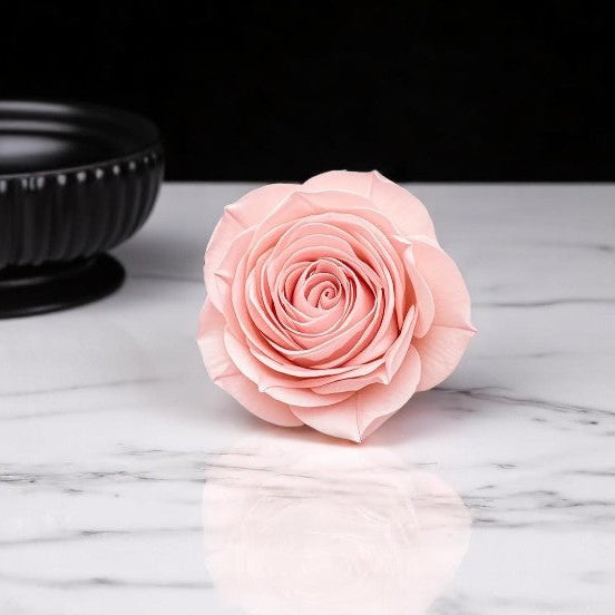 Pink wax melt rose on a marble surface with a black bowl in the background