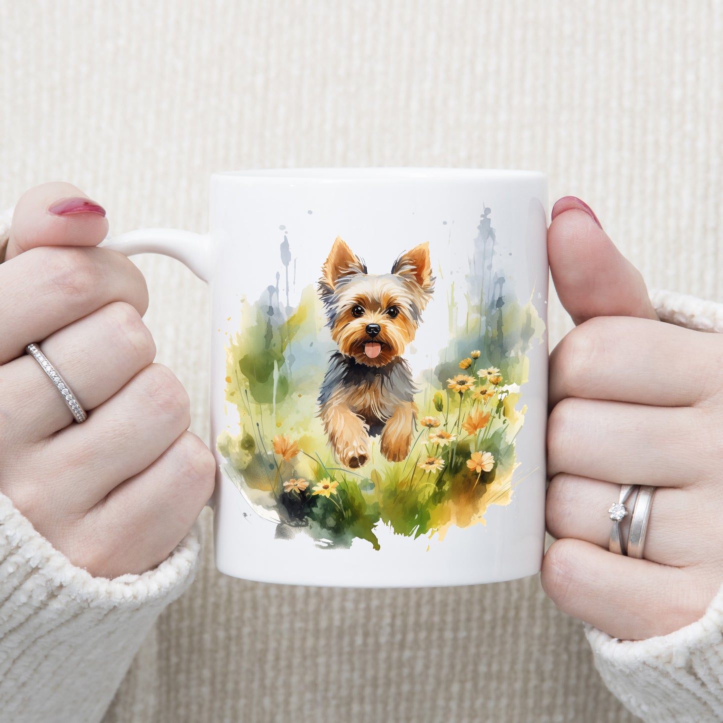 Yorkshire Terrier dog with mouth open and tongue out is running through grass and orange flowers on a white ceramic mug. The mug is being held by a woman with both hands.