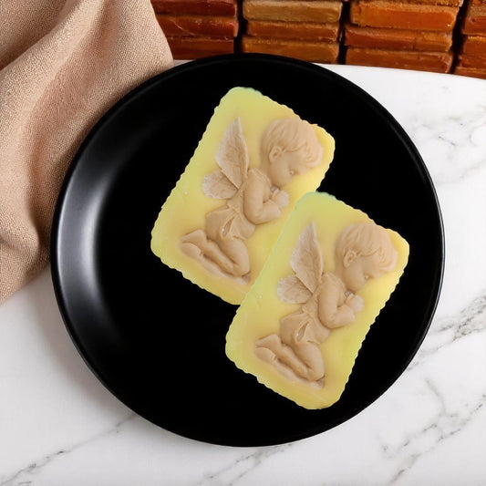 Two yellow wax melt bars with angel designs on a black plate.