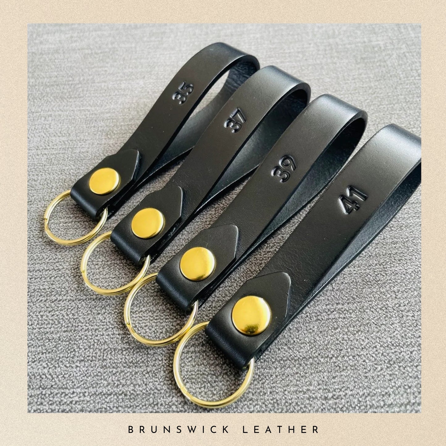 Set of black leather keychains with gold accents on a textured surface, branded 'Brunswick Leather'.