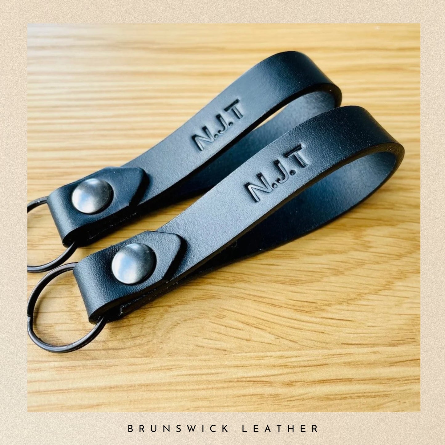 Black leather strap with 'N.J.T.' engraving on a wooden surface, branded 'Brunswick Leather'.