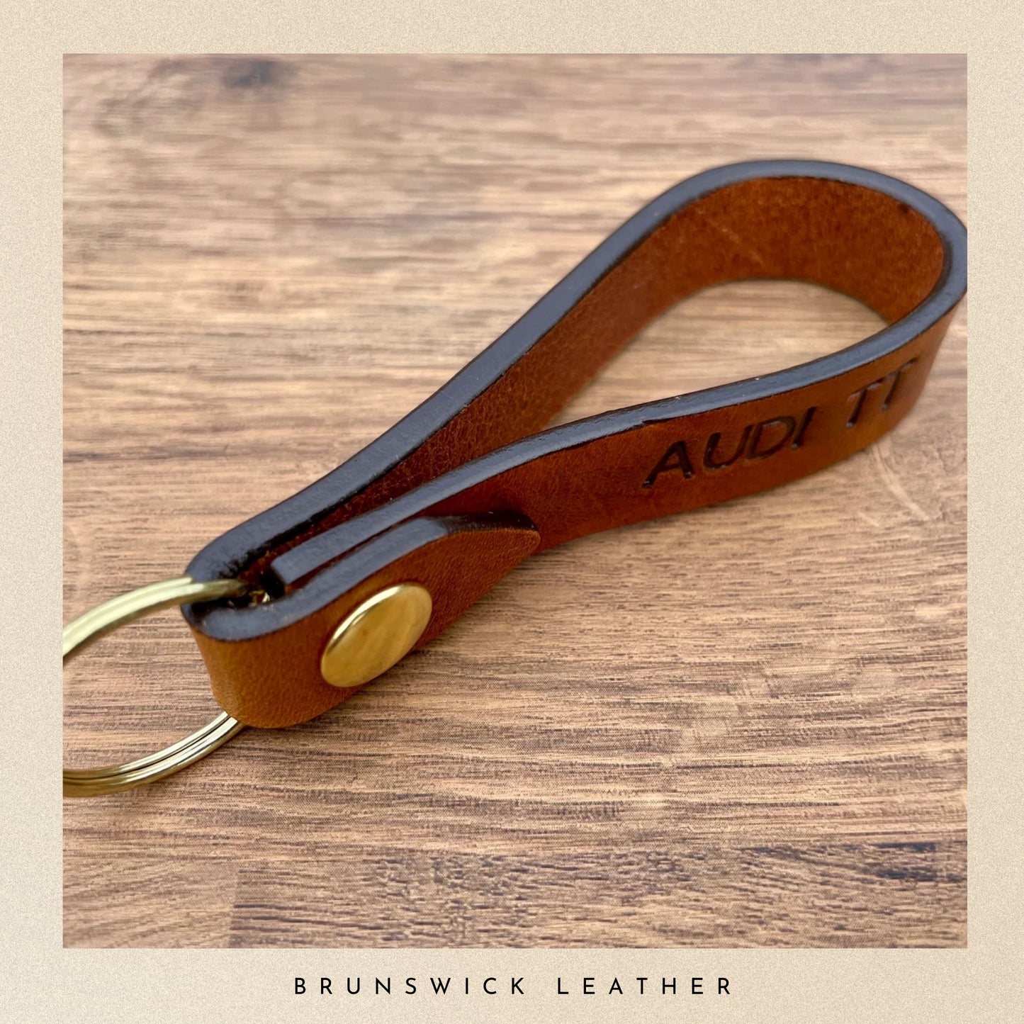 Brown leather keychain with gold accent on a wooden surface, branded 'Brunswick Leather'.