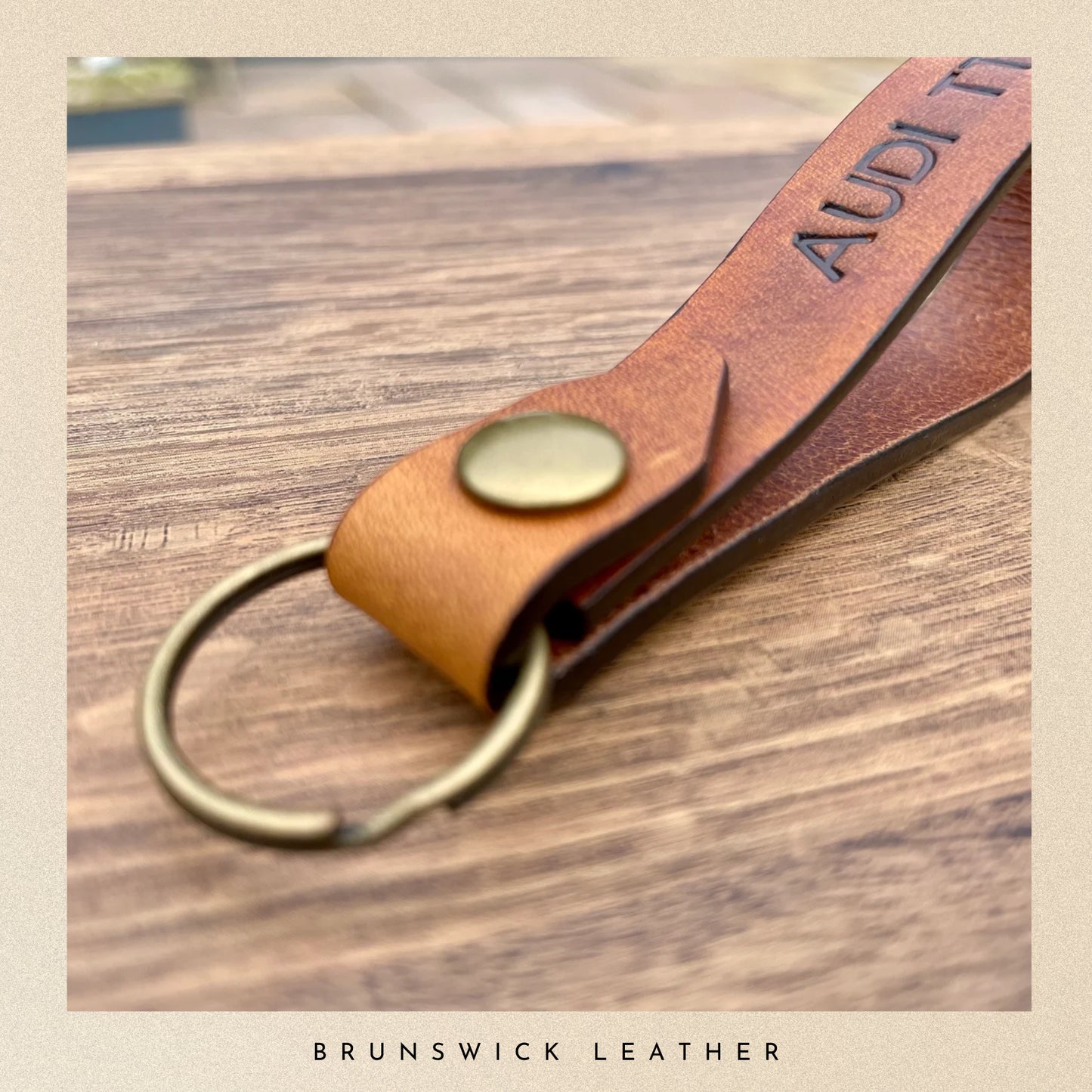 Brown leather key fob with gold accent on a wooden surface, branded 'Brunswick Leather'.