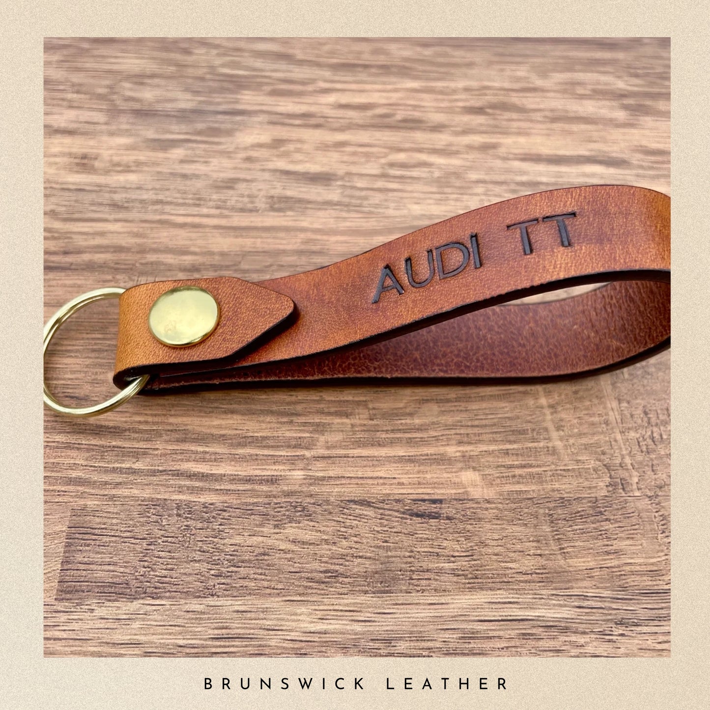 Brown leather keychain with 'Audi TT' engraving on a wooden surface, branded 'Brunswick Leather'.