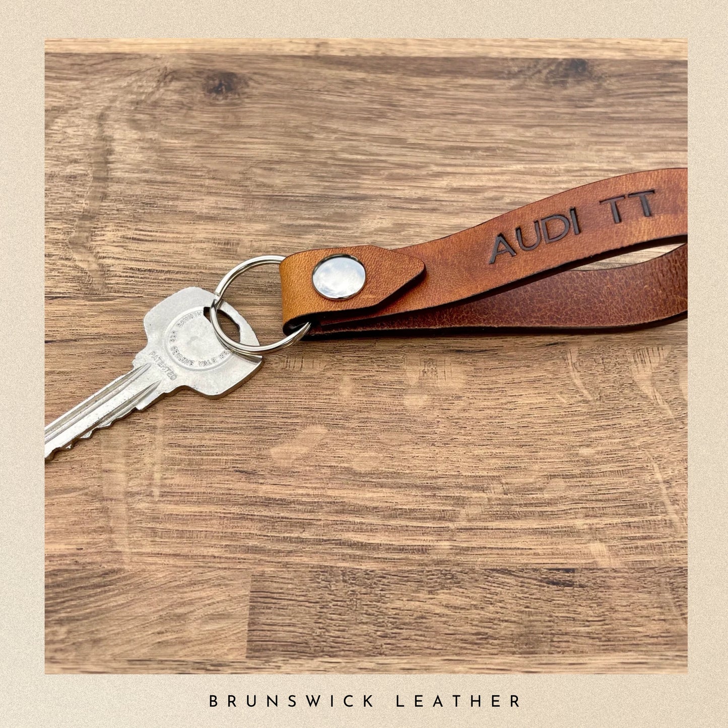 Brown leather keychain with 'Audi TT' text on a wooden surface, branded 'Brunswick Leather'.