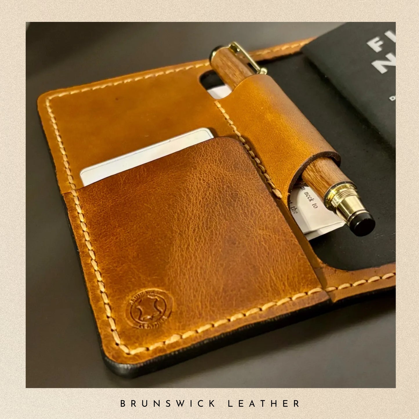 Brown leather phone case with pen and card holder on a dark surface, featuring Brunswick Leather branding.