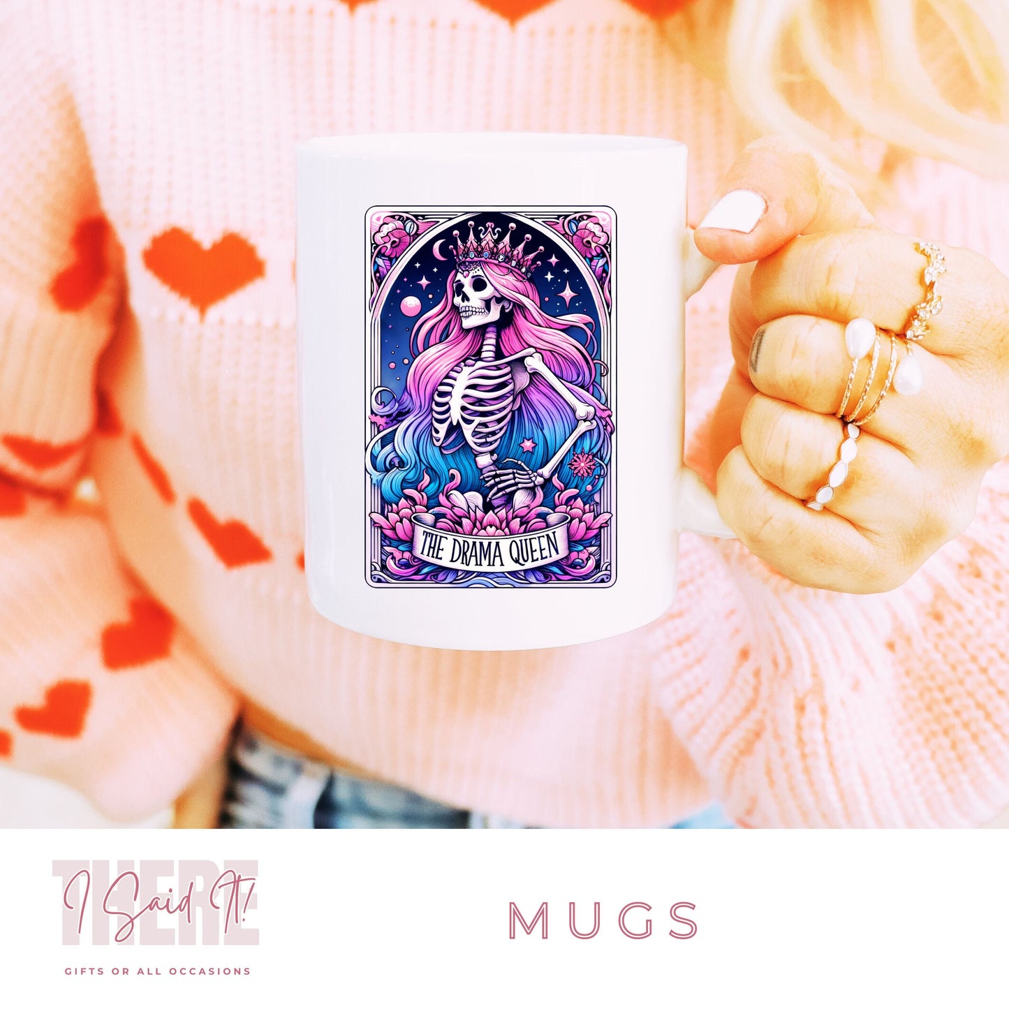 A person holding a pink coffee mug with a colourful, artistic design featuring a skeleton and hearts saying drama queen.
