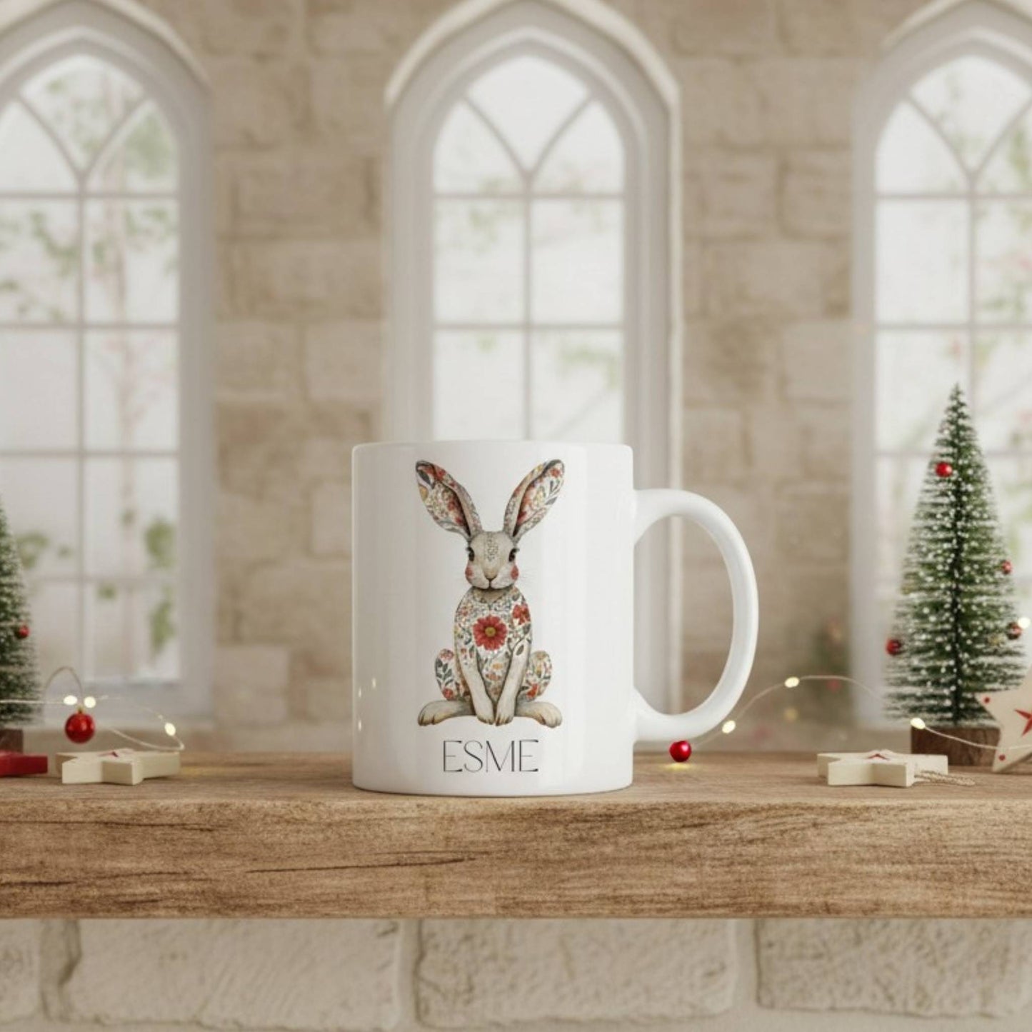 White mug with a decorative hare design and 'Esme' text on a wooden surface with festive decorations.