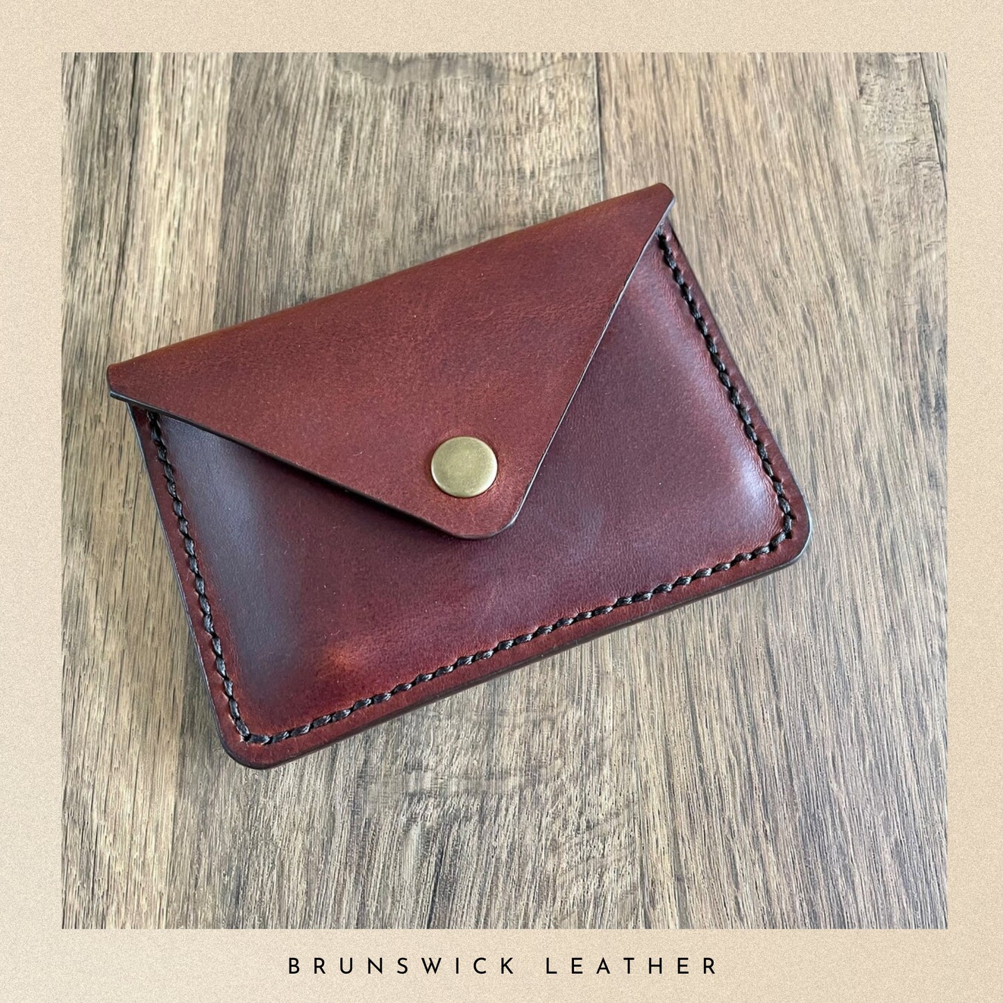 Brown leather wallet with gold button on a wooden surface, branded 'Brunswick Leather'.