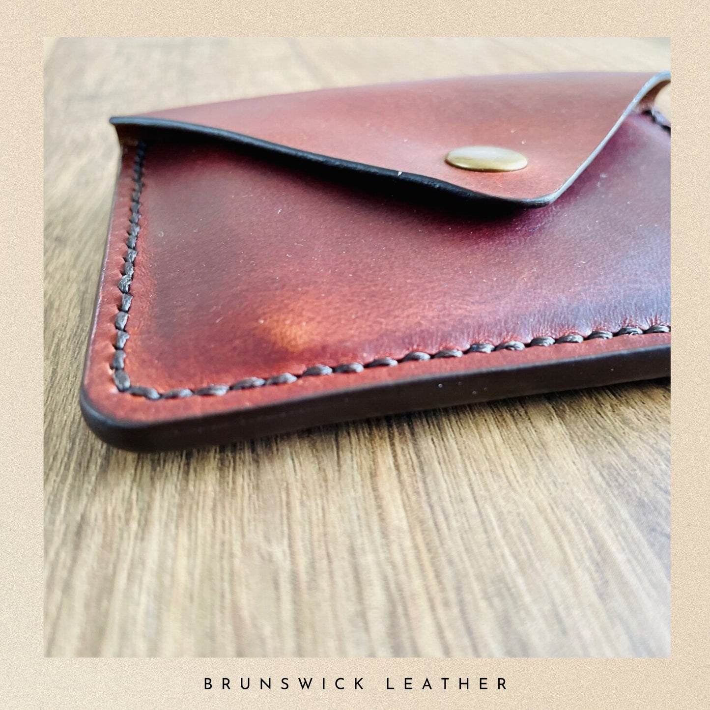 Brown leather wallet with gold clasp on a wooden surface, branded 'Brunswick Leather'.