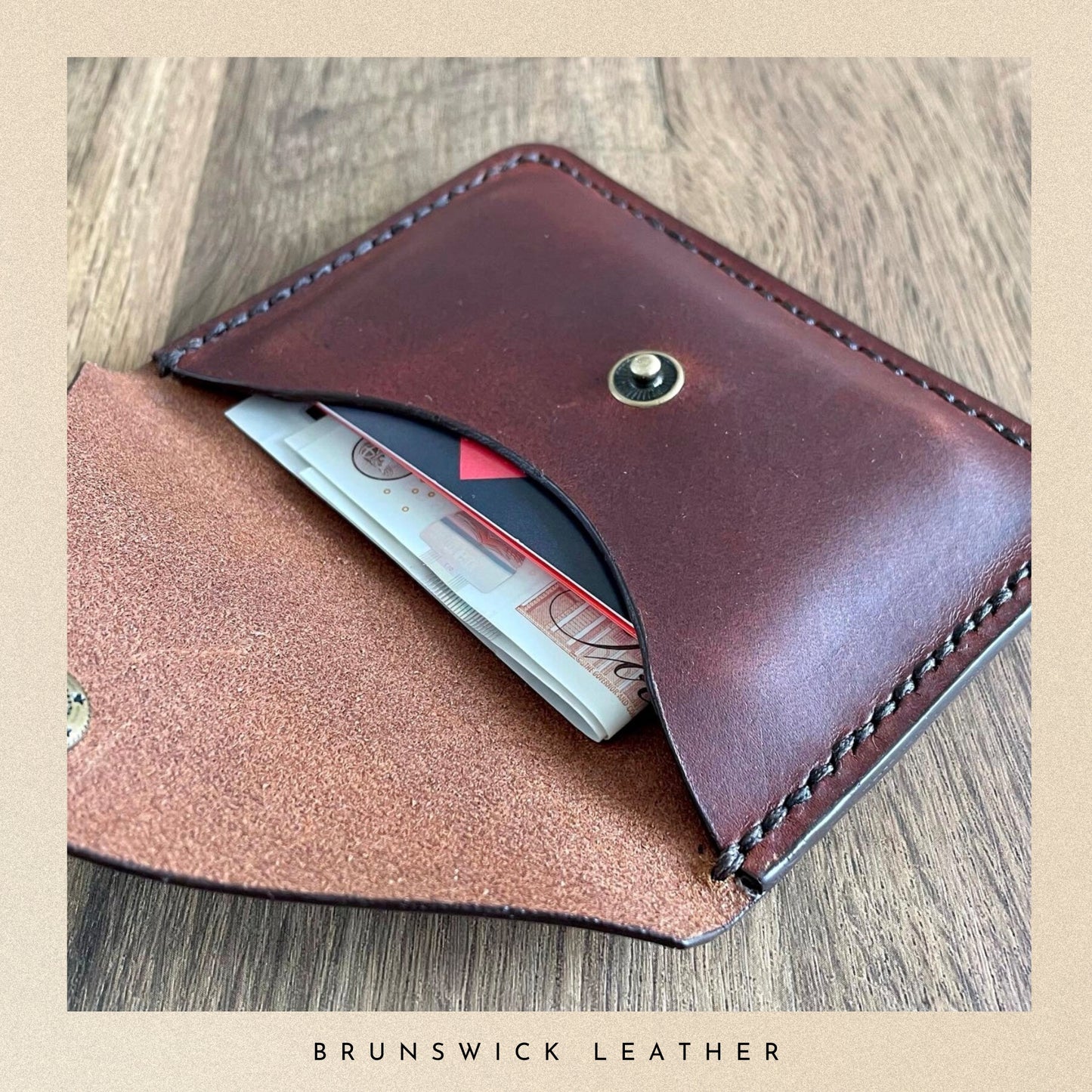 Brown leather wallet with money and cards on a wooden surface, branded 'Brunswick Leather'.