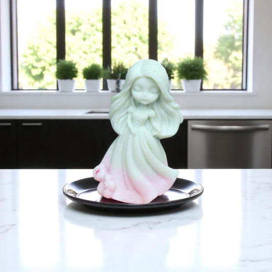 Decorative figurine of a fairy on a black plate with a window and plants in the background
