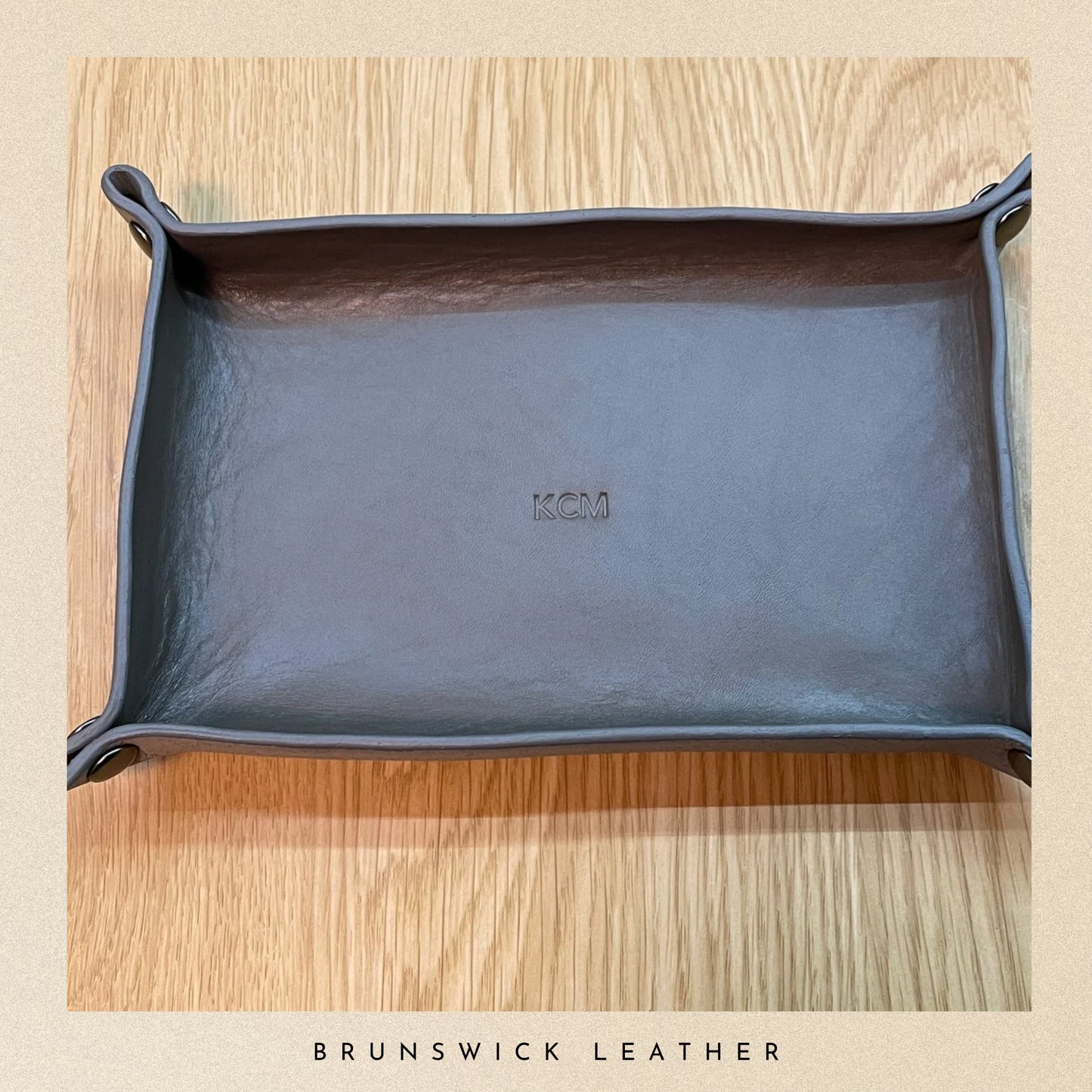 Blue leather tray with 'KMC' branding on a wooden surface, featuring the brand 'Brunswick Leather'.