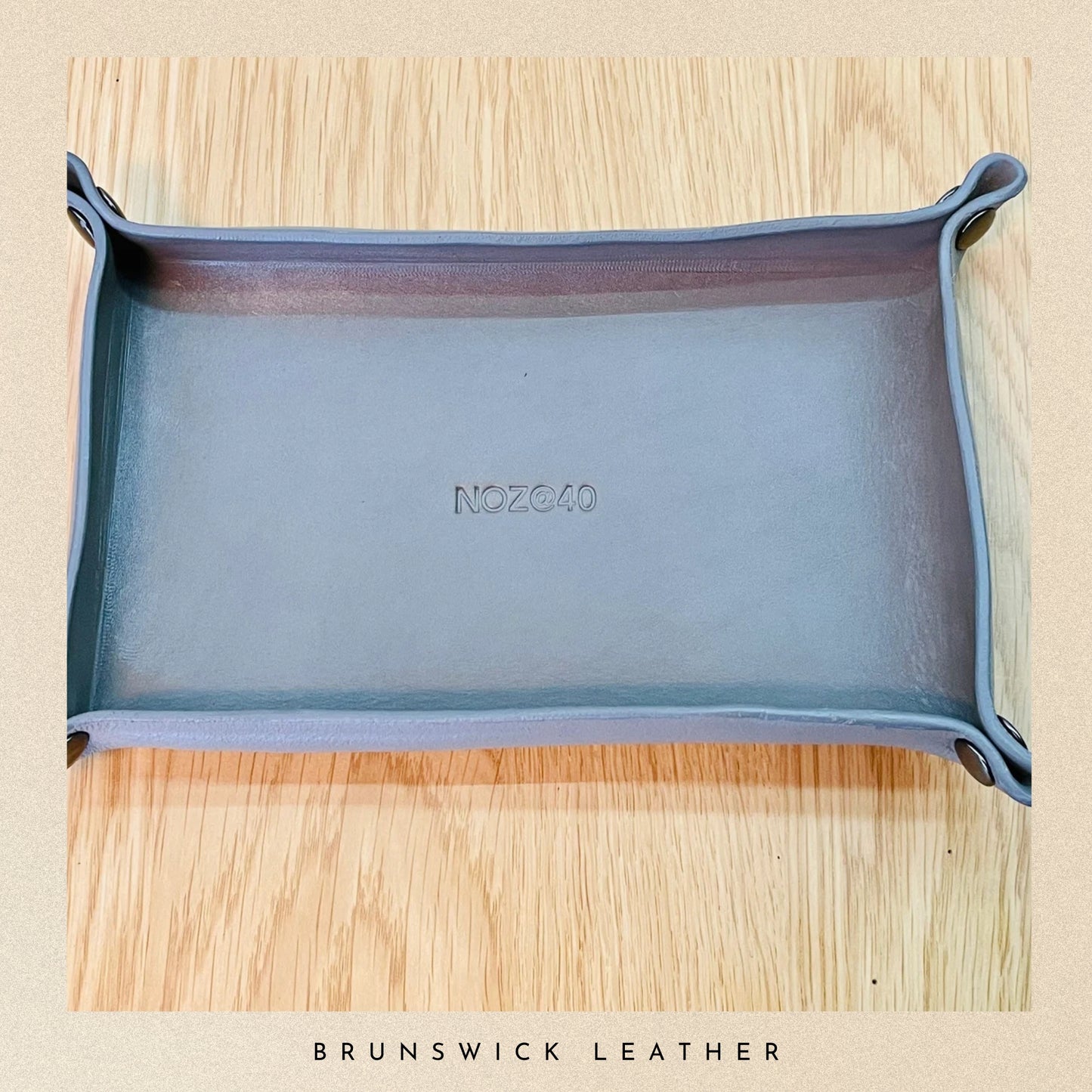 Blue leather tray with 'NOZG40' branding on a wooden surface, featuring 'Brunswick Leather' text.