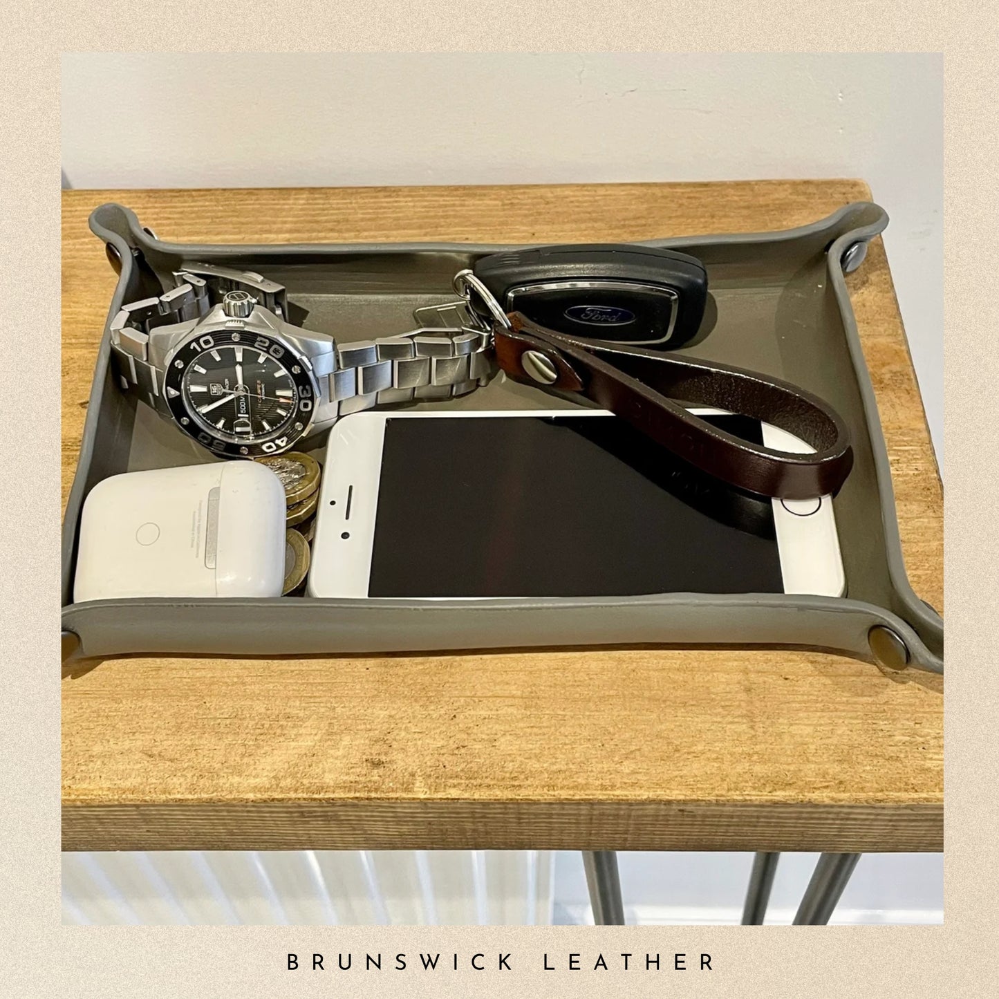 Tray with a watch, phone, and leather item on a wooden surface with 'Brunswick Leather' branding.
