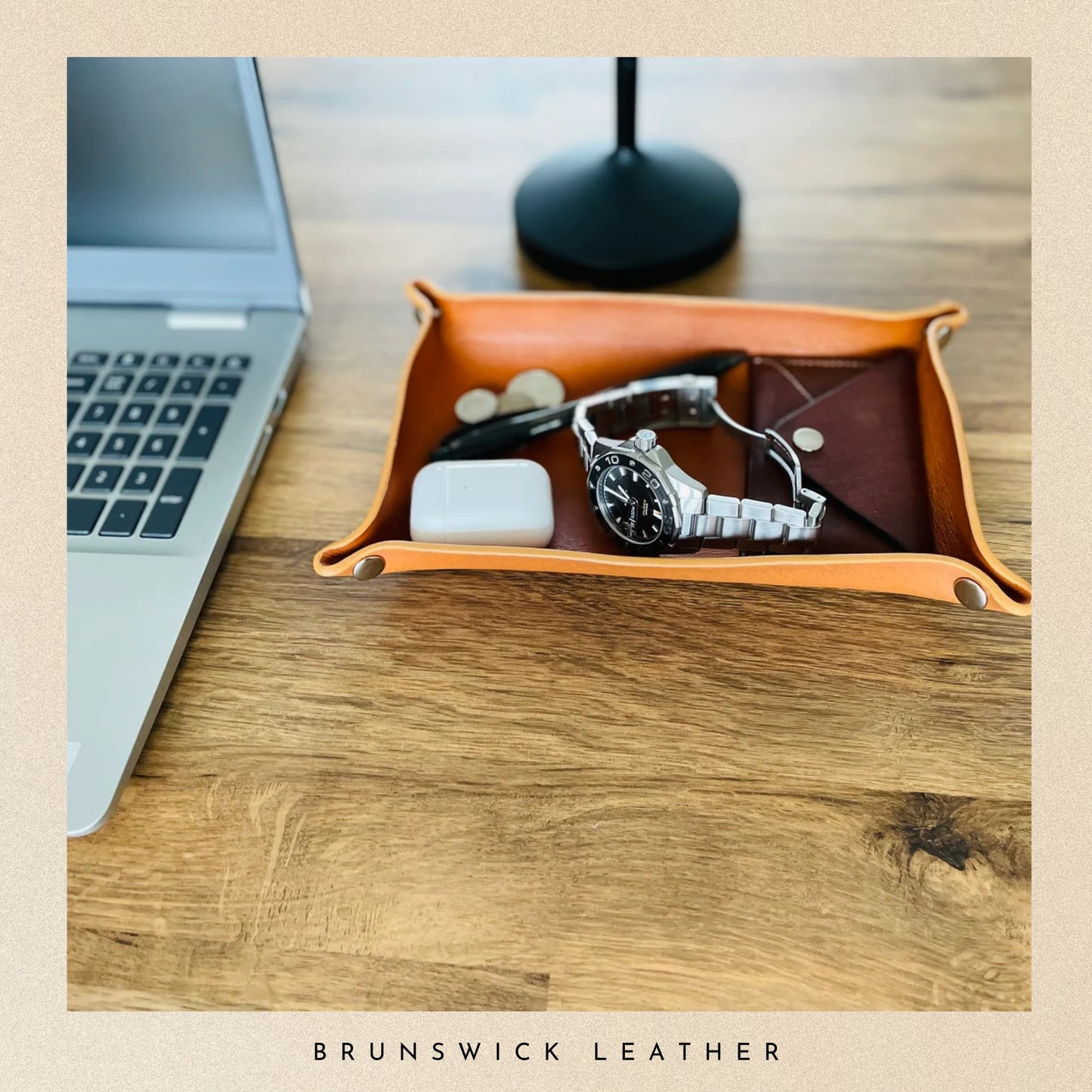 Orange leather tray with a watch, glasses, and phone on a wooden desk with 'Brunswick Leather' branding.