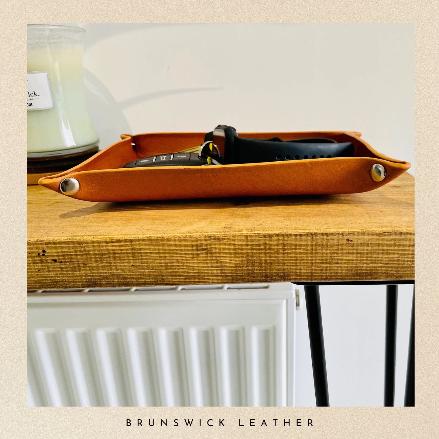 Brown leather tray on a wooden surface with a candle in the background, featuring 'Brunswick Leather' branding.
