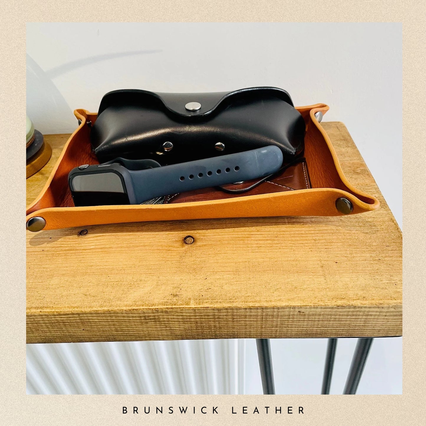 Leather tray with a black pouch and blue device on a wooden surface, branded 'Brunswick Leather'.