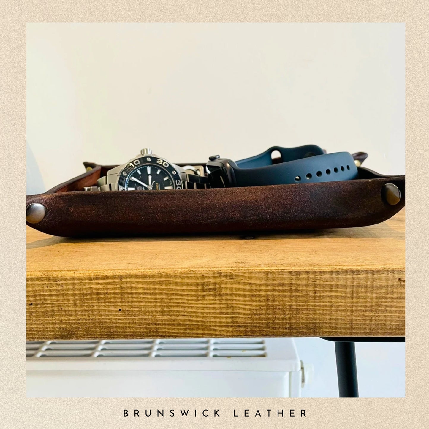 Brown leather tray with a watch and strap on a wooden surface, branded 'Brunswick Leather'.