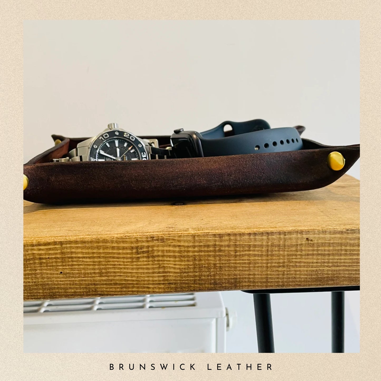 Leather tray with watches and belts on a wooden surface, branded 'Brunswick Leather'.