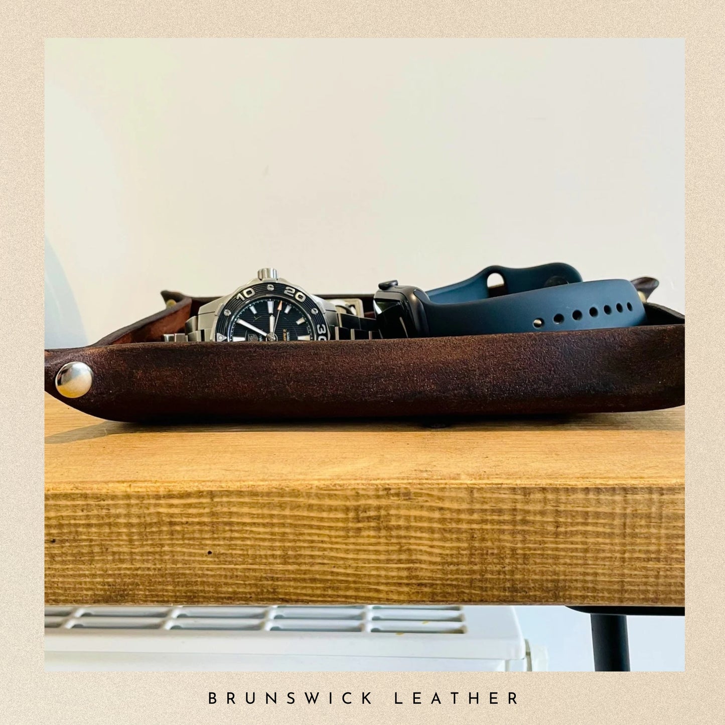 Leather tray with watch and belt on a wooden surface, branded 'Brunswick Leather'.