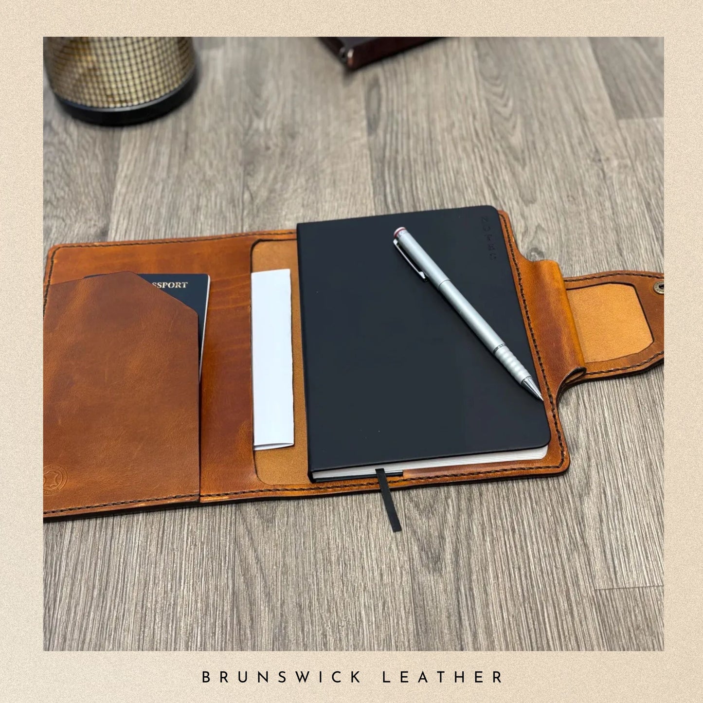 Brown leather wallet with a black notebook and pen on a wooden surface, branded 'Brunswick Leather'.
