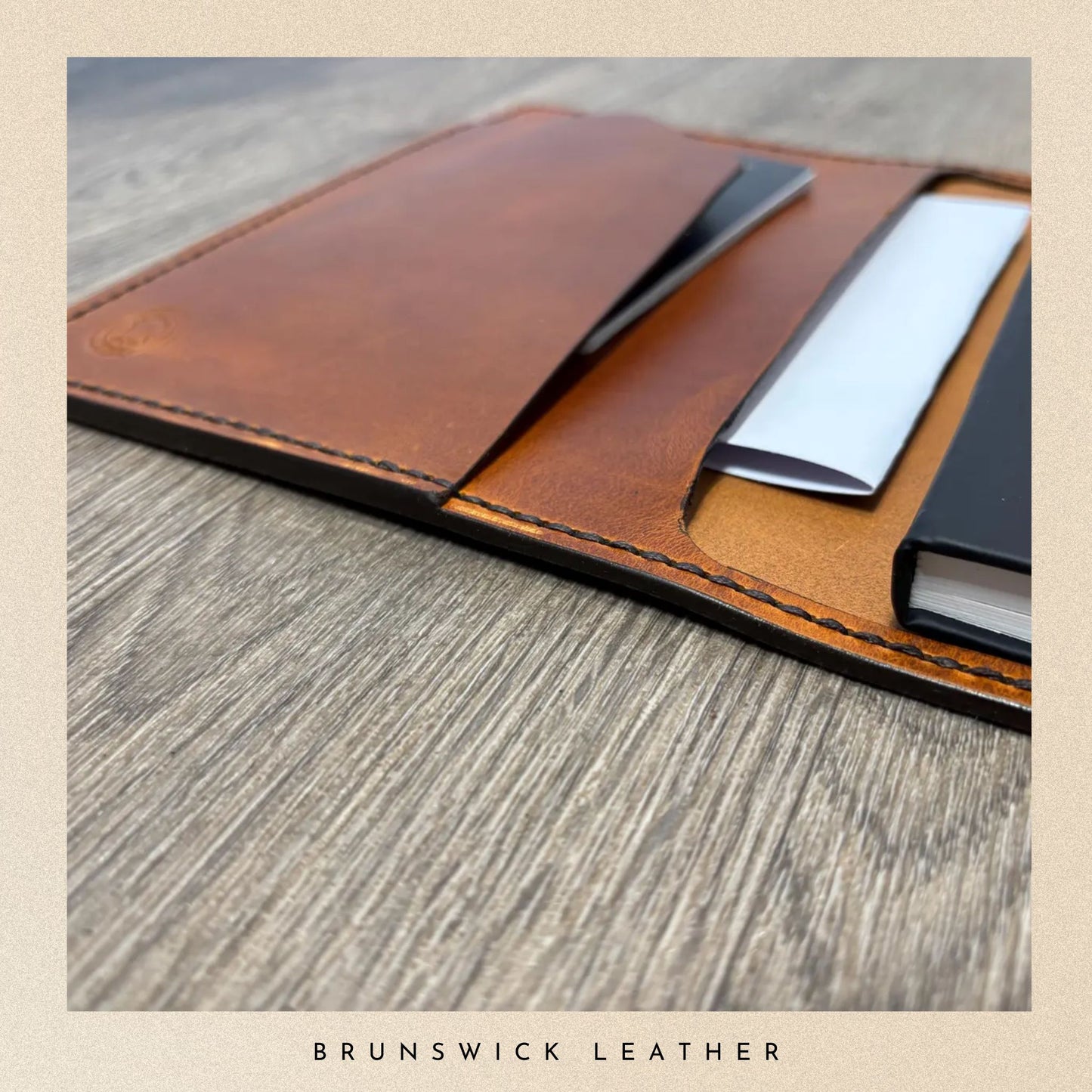 Brown leather wallet with a pen on a wooden surface, branded 'Brunswick Leather'.
