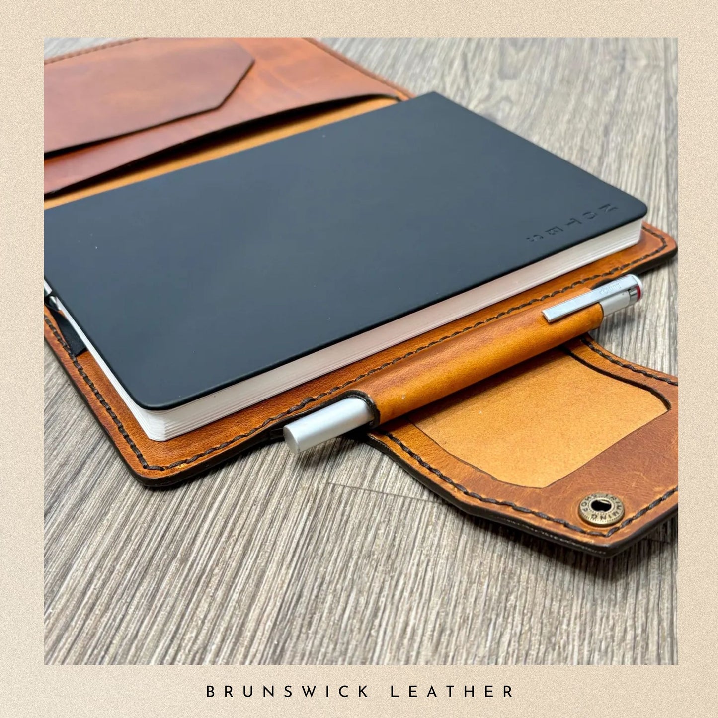 Leather notebook with pen holder on a wooden surface, featuring Brunswick Leather branding.