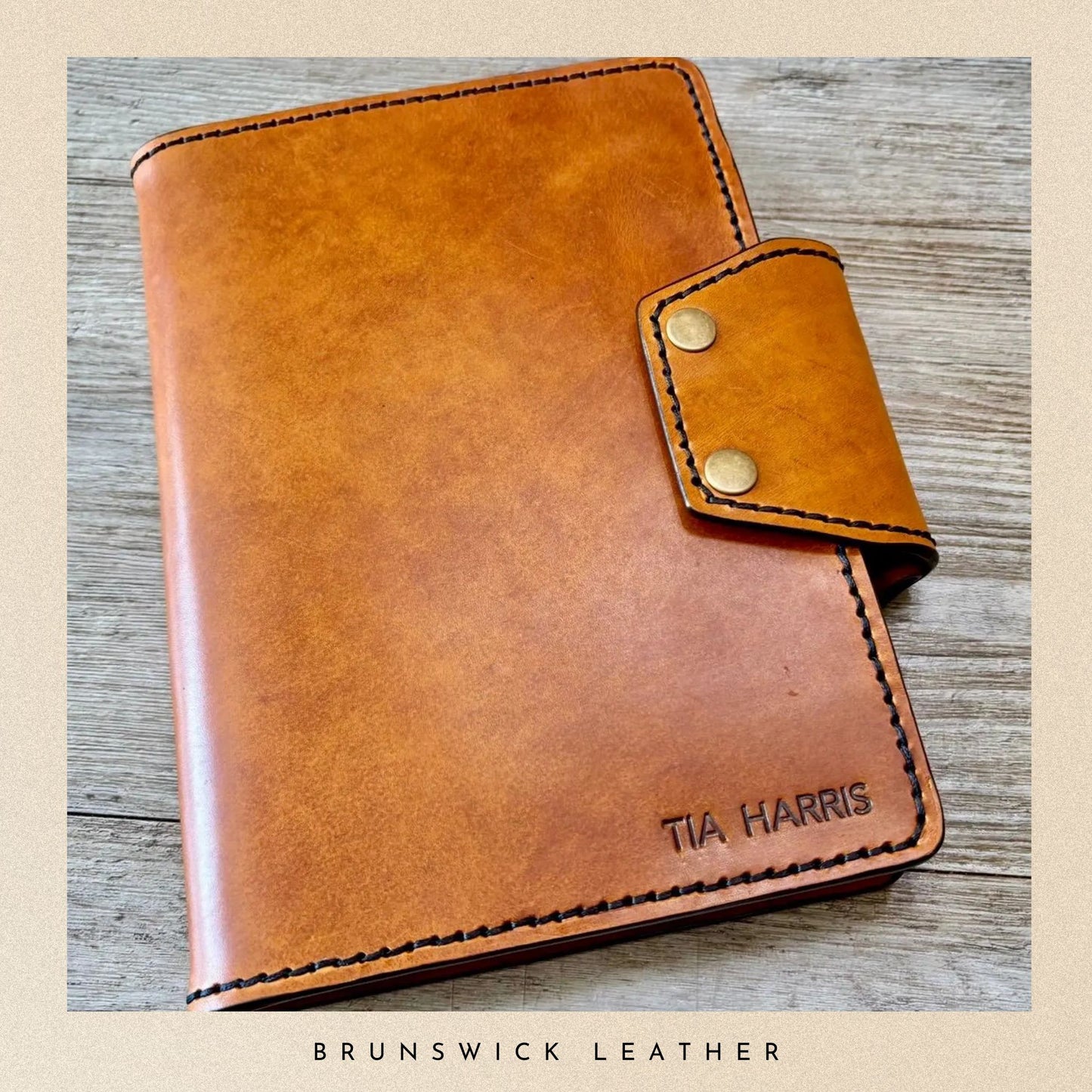 Brown leather notebook with gold accents on a wooden surface, branded 'Tia Harris' and 'Brunswick Leather'.
