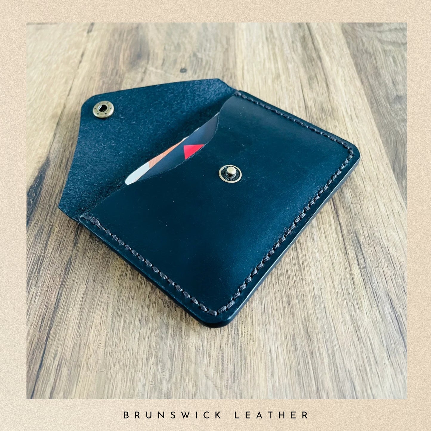 Black leather cardholder on a wooden surface with 'Brunswick Leather' branding.