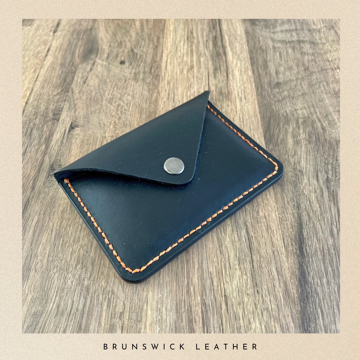 Black leather cardholder with brown stitching on a wooden surface, branded 'Brunswick Leather'.