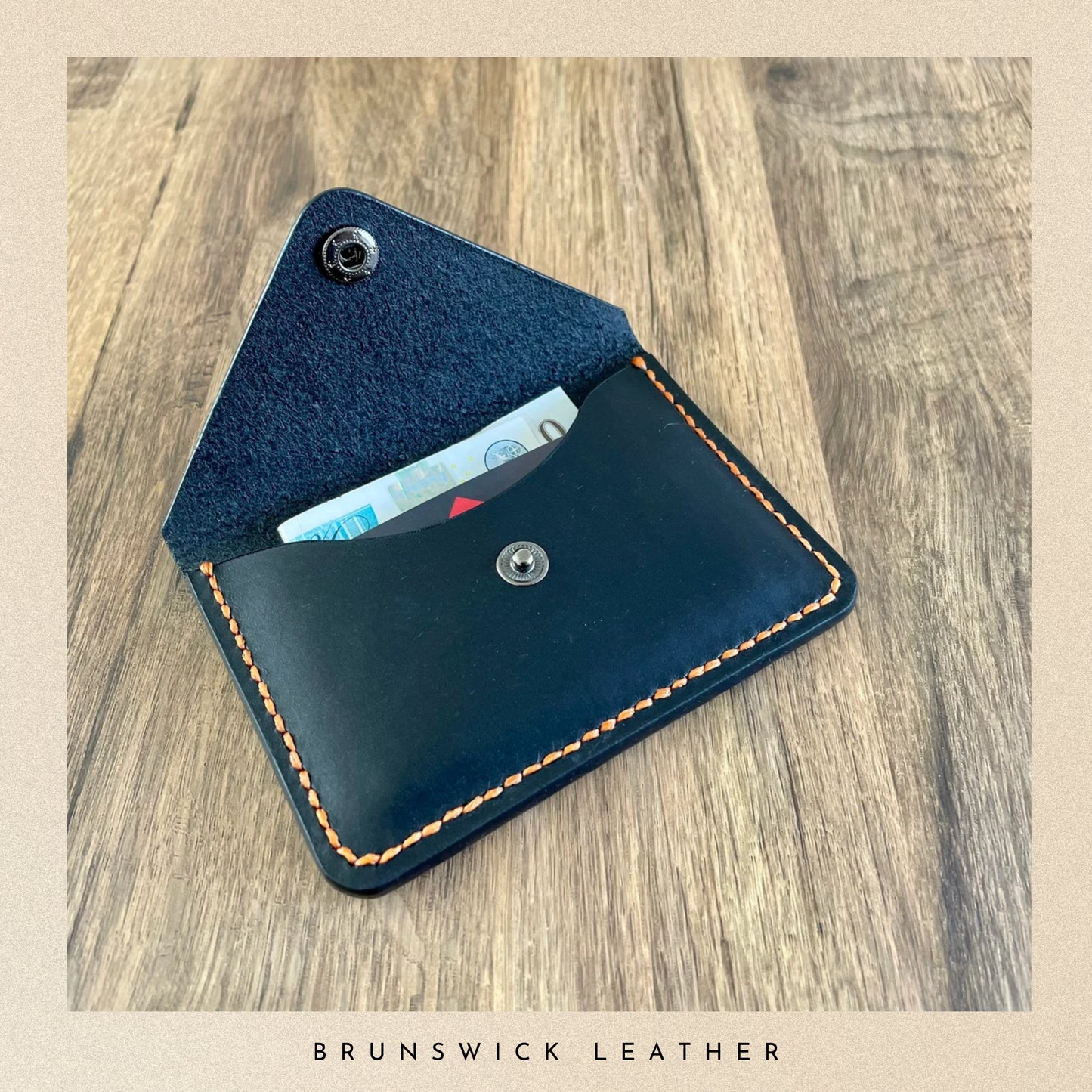Black leather wallet with stitching on a wooden surface, featuring the brand 'Brunswick Leather'.